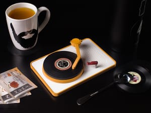 Vinyl Coaster Turntable on a dining table with mug, tea bags, spoon, and a thermos.